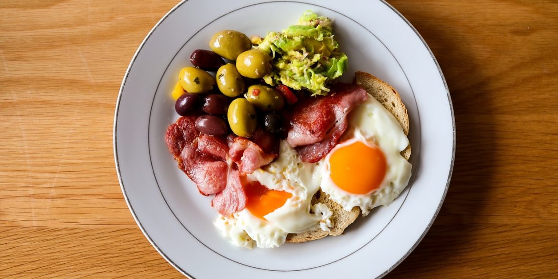 Breakfast plate with fried eggs, bacon, olives, and avocado.