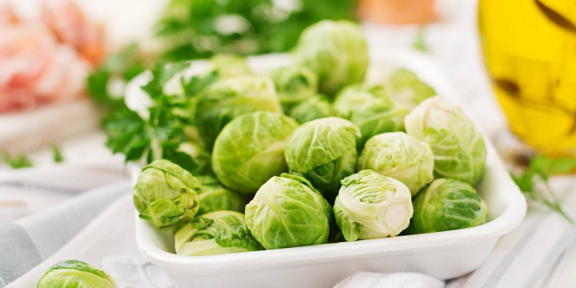 Brussels sprouts in a white dish on a table with fresh herbs.