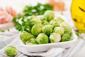 Brussels sprouts in a white dish on a table with fresh herbs.
