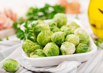 Brussels sprouts in a white dish on a table with fresh herbs.
