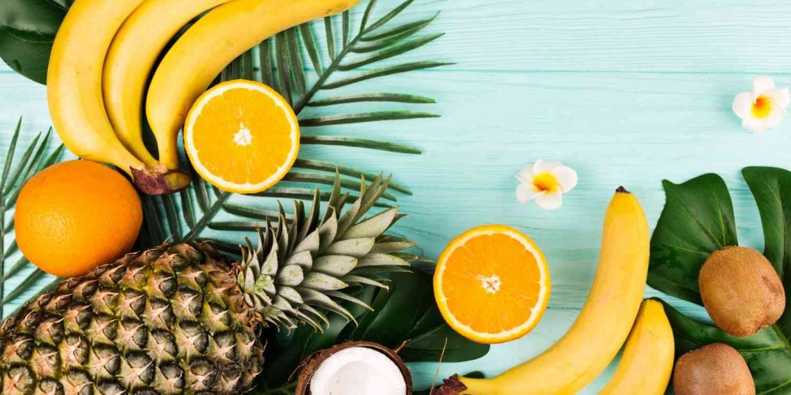 Tropical fruits like pineapple, bananas, and oranges arranged with green leaves.