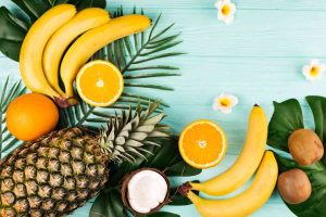 Tropical fruits like pineapple, bananas, and oranges arranged with green leaves.