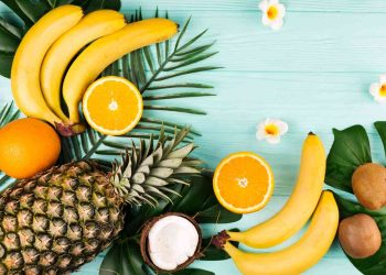 Tropical fruits like pineapple, bananas, and oranges arranged with green leaves.