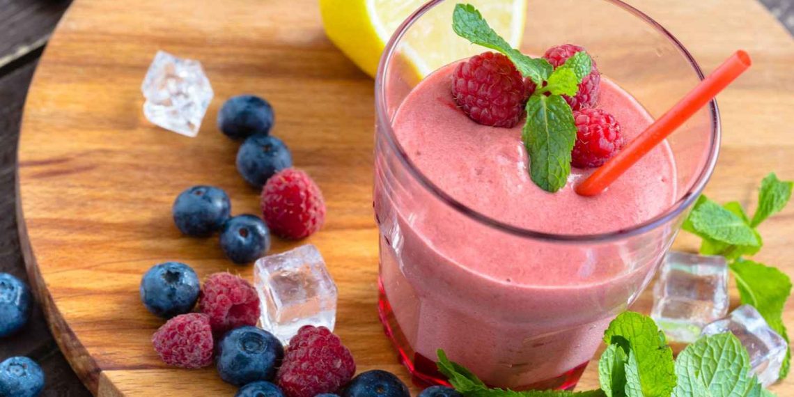 Raspberry smoothie with mint, berries, and lemon on a wooden board.
