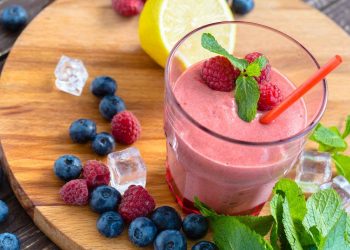 Raspberry smoothie with mint, berries, and lemon on a wooden board.