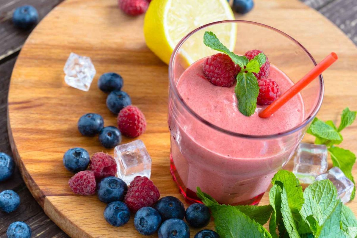 Raspberry smoothie with mint, berries, and lemon on a wooden board.