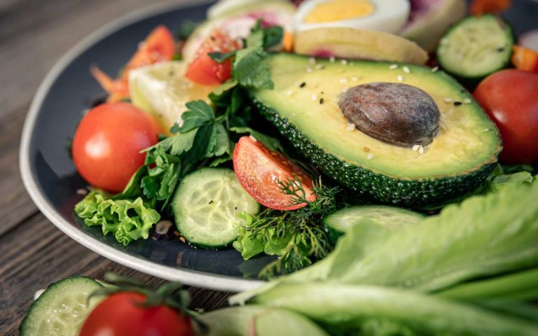 Avocado salad with fresh tomatoes, cucumbers, and herbs on a plate.