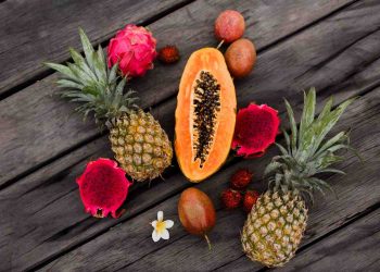 Tropical fruits arranged on a wooden table, including papaya, pineapples, and dragon fruit.