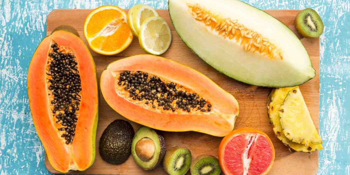 Tropical fruits arrangement with papaya, avocado, and citrus slices on a wooden board.
