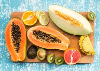 Tropical fruits arrangement with papaya, avocado, and citrus slices on a wooden board.