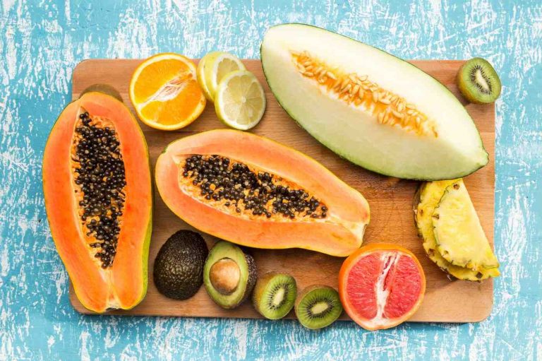 Tropical fruits arrangement with papaya, avocado, and citrus slices on a wooden board.