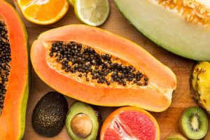 Tropical fruits including papaya, avocado, and citrus slices arranged on a wooden board.