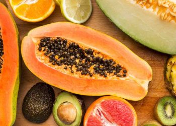 Tropical fruits including papaya, avocado, and citrus slices arranged on a wooden board.