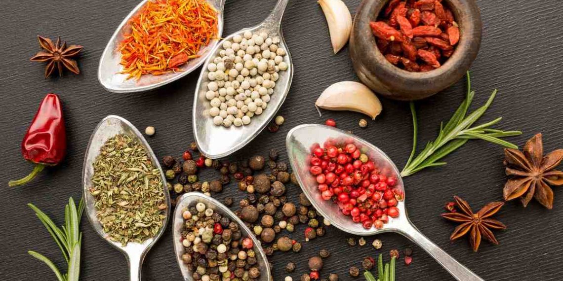 Spoons filled with diverse spices and herbs on black background.