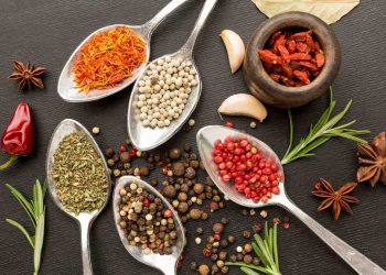 Spoons filled with diverse spices and herbs on black background.