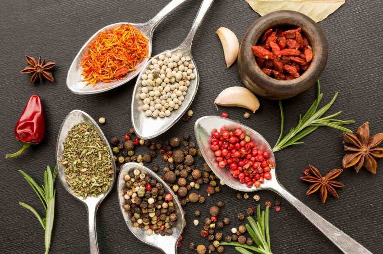 Spoons filled with diverse spices and herbs on black background.