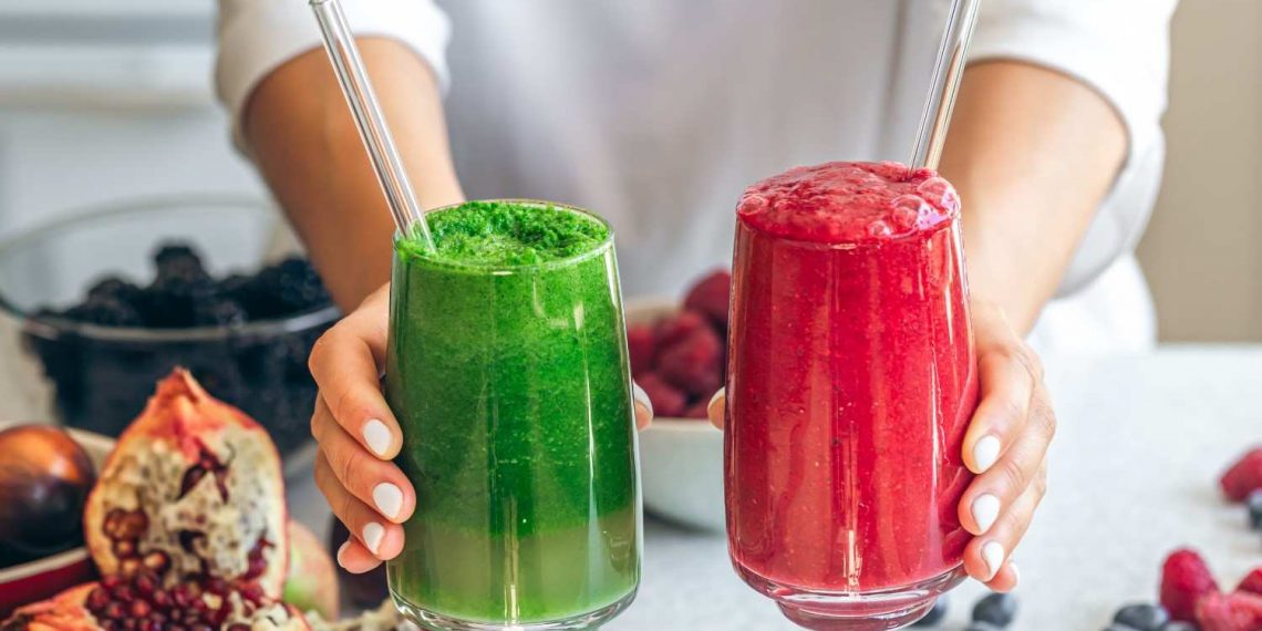 Hands holding green and red smoothies with fresh berries and pomegranates.