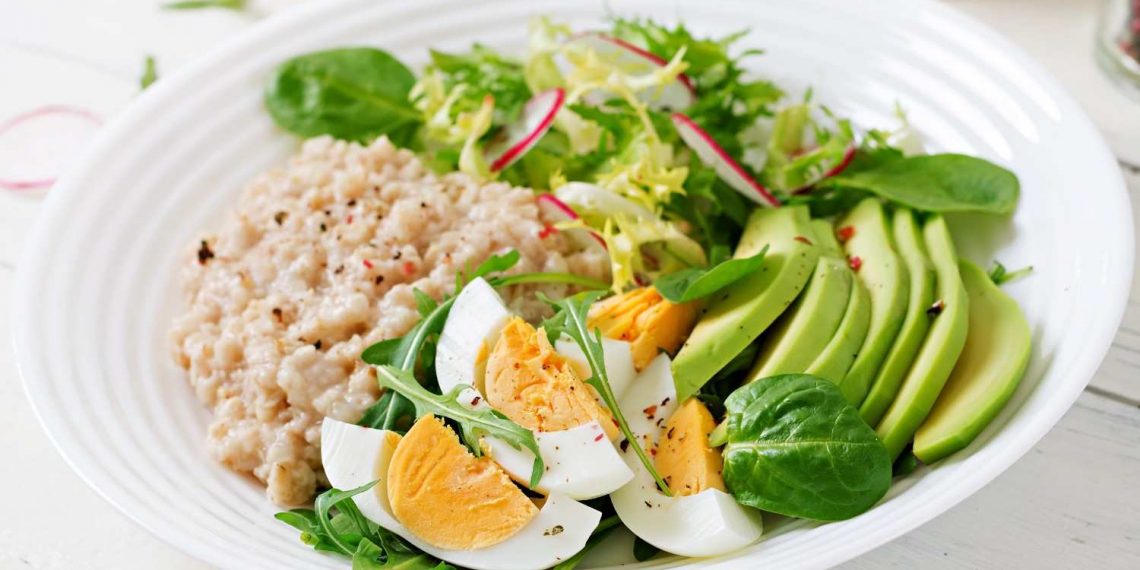 Healthy breakfast bowl with eggs, avocado, greens, and oatmeal.