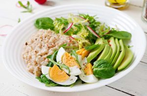 Healthy breakfast bowl with eggs, avocado, greens, and oatmeal.