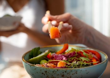Chopsticks lifting fresh salmon from colorful poke bowl.