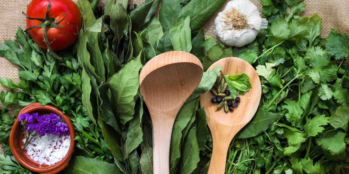 Fresh herbs and vegetables with wooden spoons on burlap.