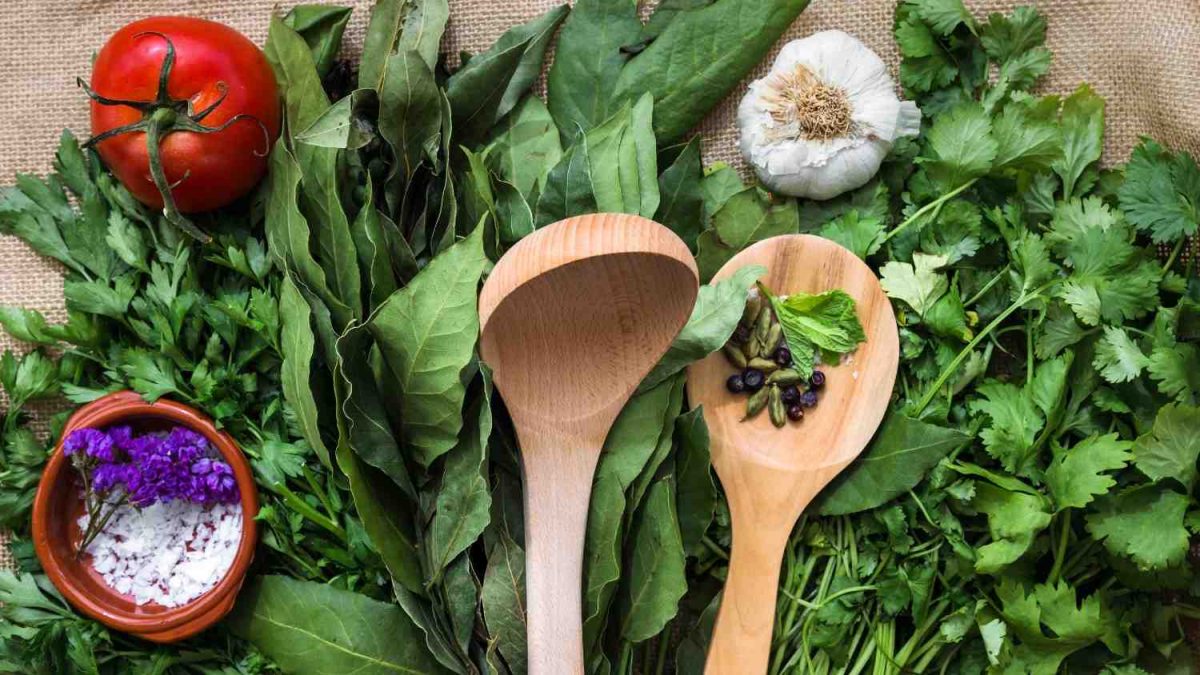 Fresh herbs and vegetables with wooden spoons on burlap.