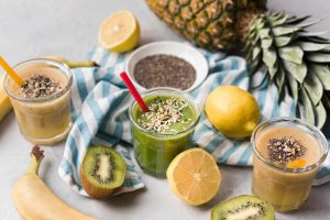 Three healthy smoothies with chia seeds, surrounded by fresh fruits.