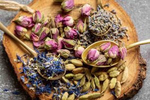 Dried rosebuds, lavender, blue petals, cardamom on wood slice with spoons.