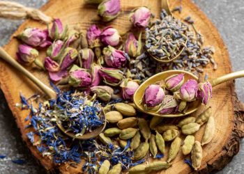 Dried rosebuds, lavender, blue petals, cardamom on wood slice with spoons.