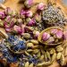 Dried rosebuds, lavender, blue petals, cardamom on wood slice with spoons.