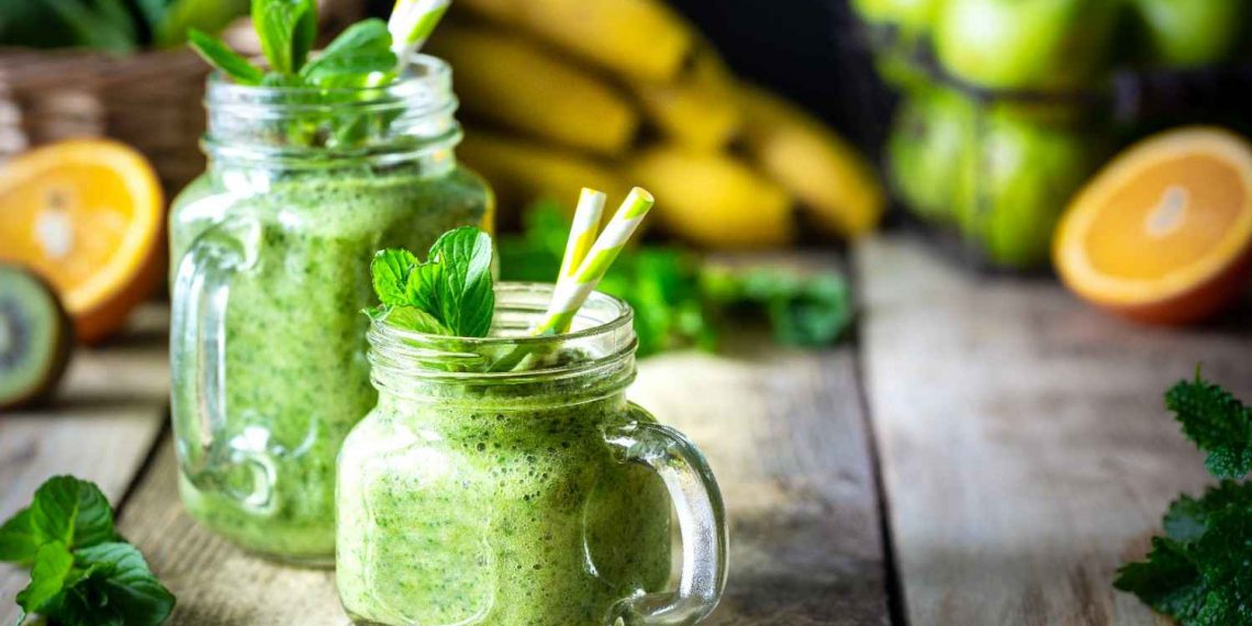 Green smoothie in mason jars with fresh mint and fruits.