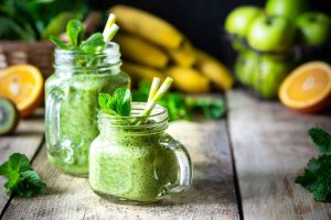 Green smoothie in mason jars with fresh mint and fruits.