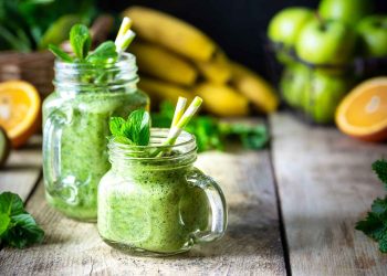 Green smoothie in mason jars with fresh mint and fruits.