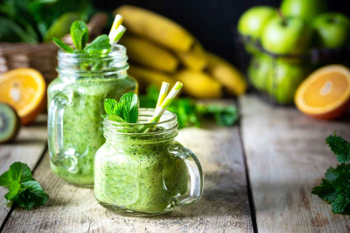 Green smoothie in mason jars with fresh mint and fruits.