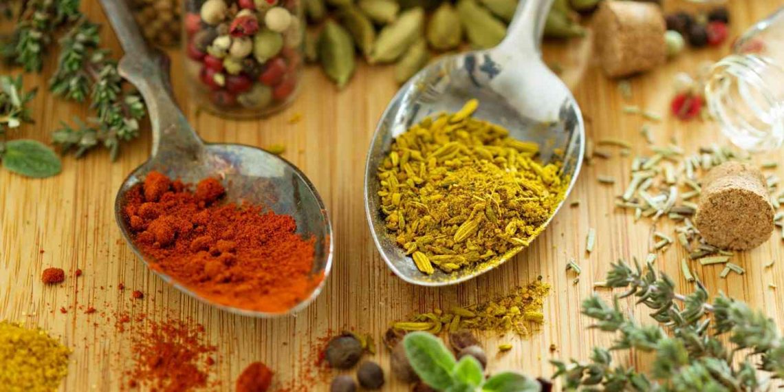 Spoons with colorful spices on wooden surface.