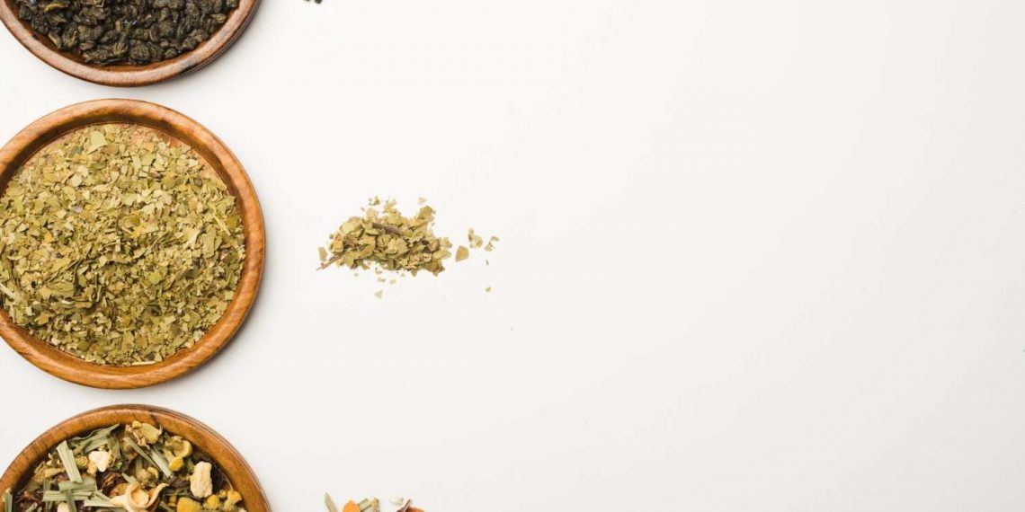 Assorted loose-leaf teas in wooden bowls on a white background.