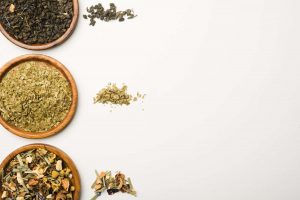 Assorted loose-leaf teas in wooden bowls on a white background.