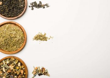 Assorted loose-leaf teas in wooden bowls on a white background.