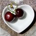 Two cherries in a heart-shaped bowl on a textured surface.