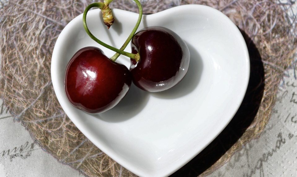 Two cherries in a heart-shaped bowl on a textured surface.