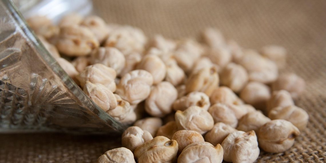 Chickpeas spilling from a glass jar on burlap.