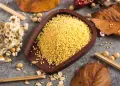 Millet grains in a wooden bowl surrounded by autumn leaves and flowers.