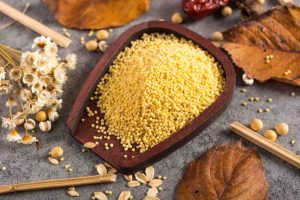 Millet grains in a wooden bowl surrounded by autumn leaves and flowers.