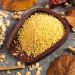Millet grains in a wooden bowl surrounded by autumn leaves and flowers.