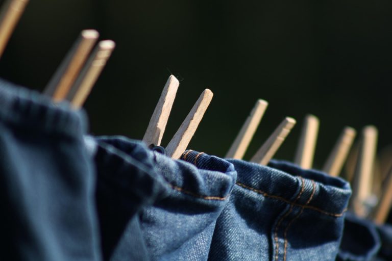 Jeans drying on a clothesline with wooden clothespins.
