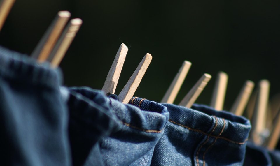 Jeans drying on a clothesline with wooden clothespins.
