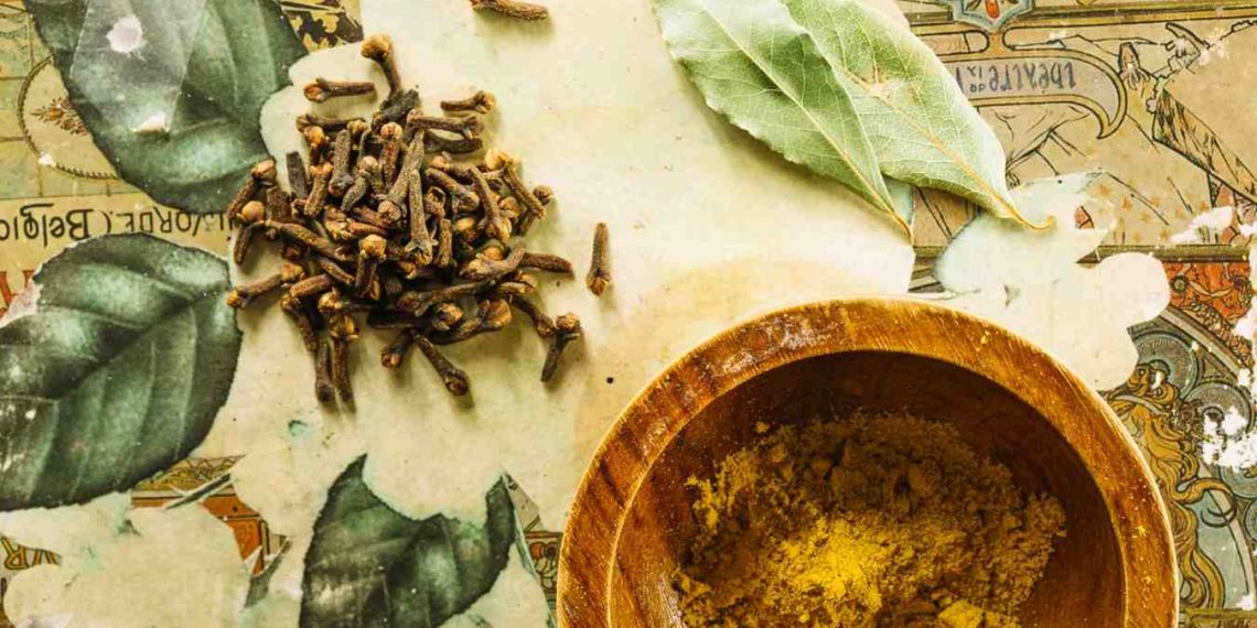 Cloves and bay leaves with curry powder in a wooden bowl.