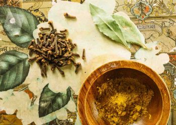 Cloves and bay leaves with curry powder in a wooden bowl.