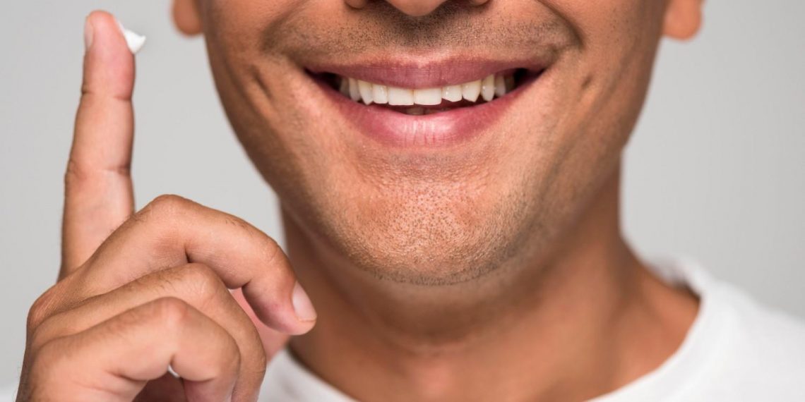 Man smiling, holding cream on finger close to face