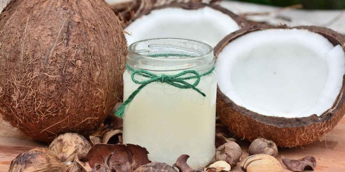 Coconut oil in a glass jar surrounded by fresh coconuts.